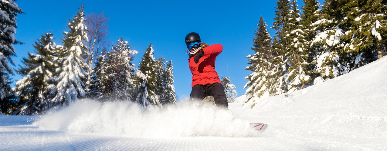 Tjej på snowboard som sprutar upp snö med brädan