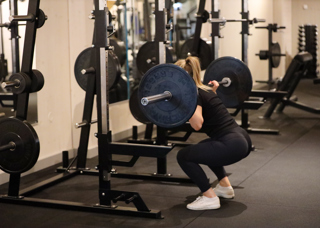 Ung tjej gör benböj med viktstång på X-gym i Orsa Grönklitt - träning i vacker miljö.
