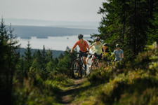 Ungdommar som cyklar på skogsstig med vy över Orsasjön i Orsa Grönklitt.