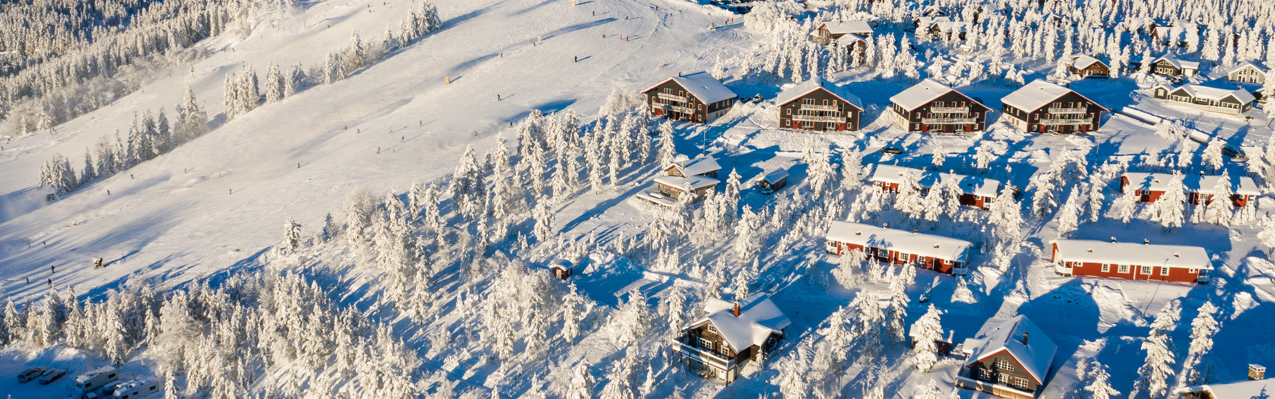 Vy över stugor och slalombackar i Orsa Grönklitt, träd och mark är täckta av snö
