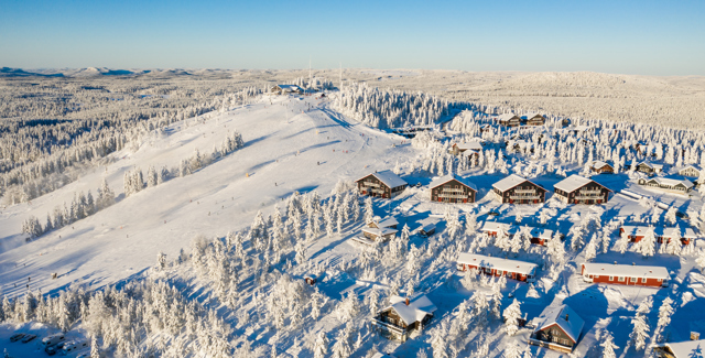 Vy över stugor och slalombackar i Orsa Grönklitt, träd och mark är täckta av snö
