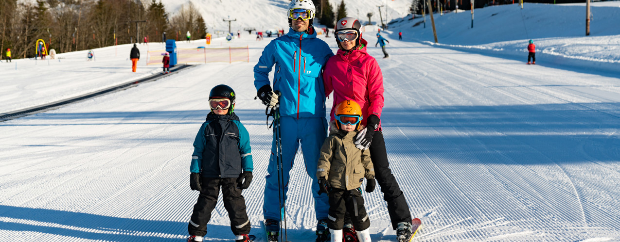 Familj på slalomskidor som står tillsammans nedanför en alpinbacke i Orsa Grönklitt