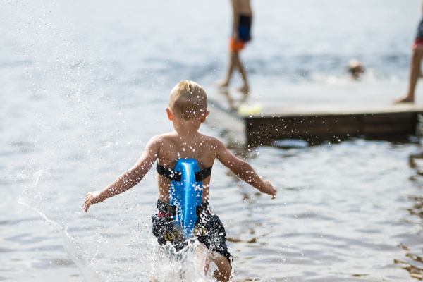 Pojke som springer ut i vattnet från sandstranden i Rädsjön i Orsa Grönklitt