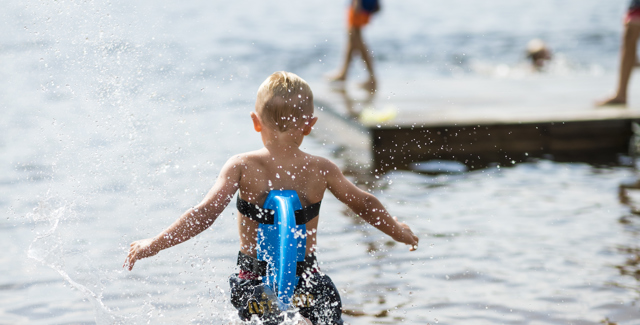 Pojke som springer ut i vattnet från sandstranden i Rädsjön i Orsa Grönklitt