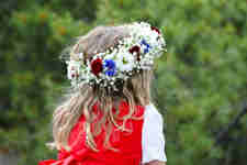 A little girl celebrating Midsummer wearing a traditional dress and a flower wreath on her head.