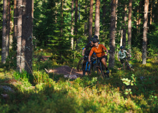 Tre personer njuter av mountainbiking i Orsa Grönklitts skogar - en spännande äventyrsupplevelse i naturen.