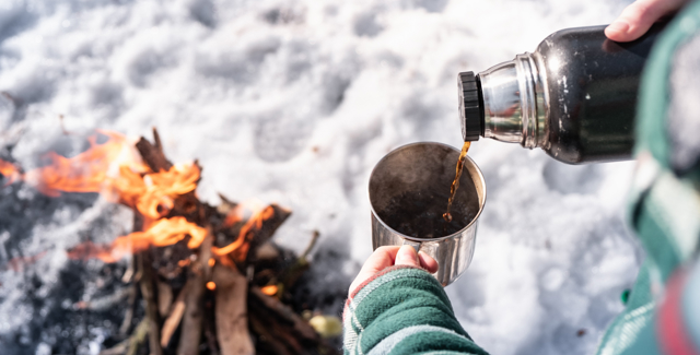 Kvinna som dricker kaffe ur termos över öppen eld i Orsa Grönklitt
