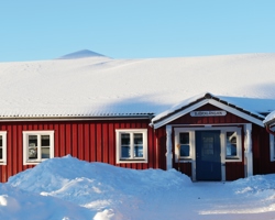 Röd byggnad med blå dörr i snötäckt landskap - vandrarhem Orsa Grönklitt