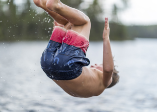 Modigt barn hoppar bakåtvolt i Rädsjön från bryggan i Orsa Grönklitt.